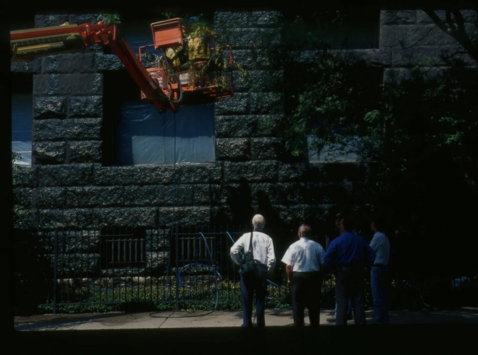 Four people stand on a sidewalk in front of the Newberry. A cherry-picker crane extends out from the left.