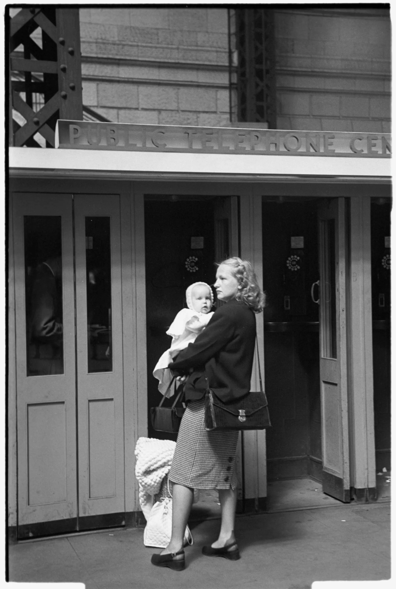 A mother holding her infant child in front of a row of train station telephone booths