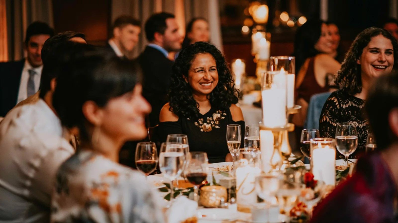 People sit at tables in a banquet room. They are smiling and laughing.