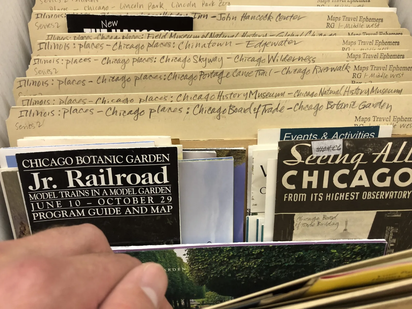 A hand leafs through archival folders filled with Chicago travel ephemera.